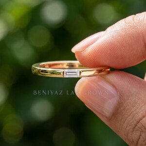 Close up hand held baguette lab grown diamond band showing the horizontal stone setting and slim gold profile.