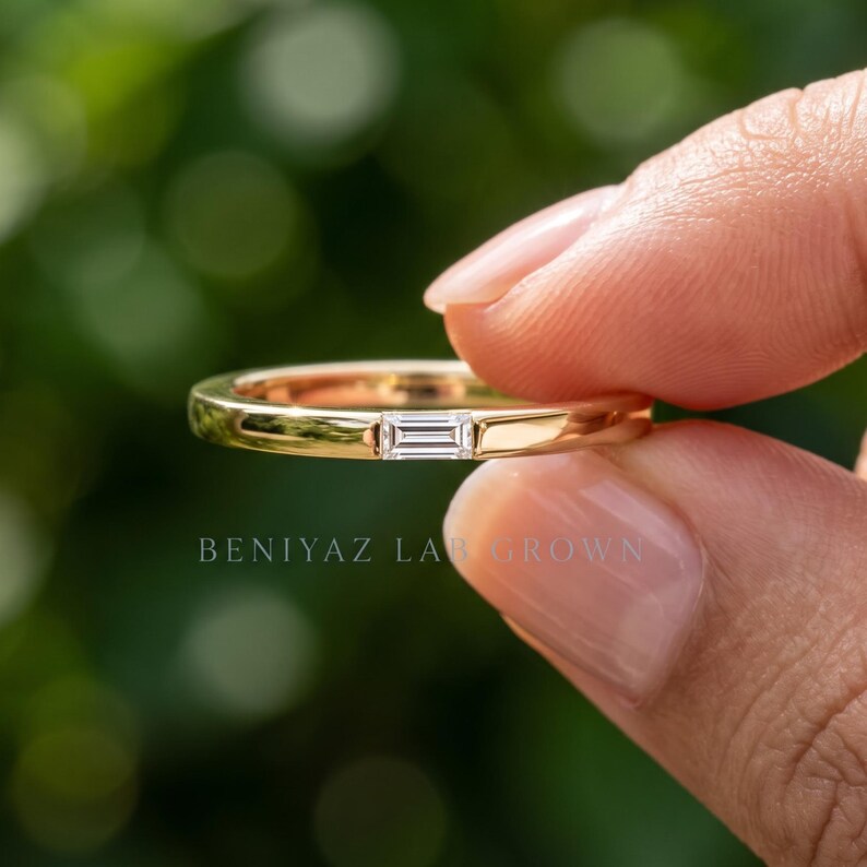 Close up hand held baguette lab grown diamond band showing the horizontal stone setting and slim gold profile.