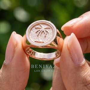 Close up hand view of a rose gold vermeil palm tree signet ring featuring a round textured medallion face and tapered statement band