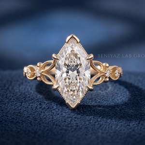 May include: A gold ring featuring a large marquise-cut center stone held by six prongs. The band displays intricate filigree metalwork and small round accent stones on both sides. The text BENIYAZ LAB GRO is visible in the upper right corner.