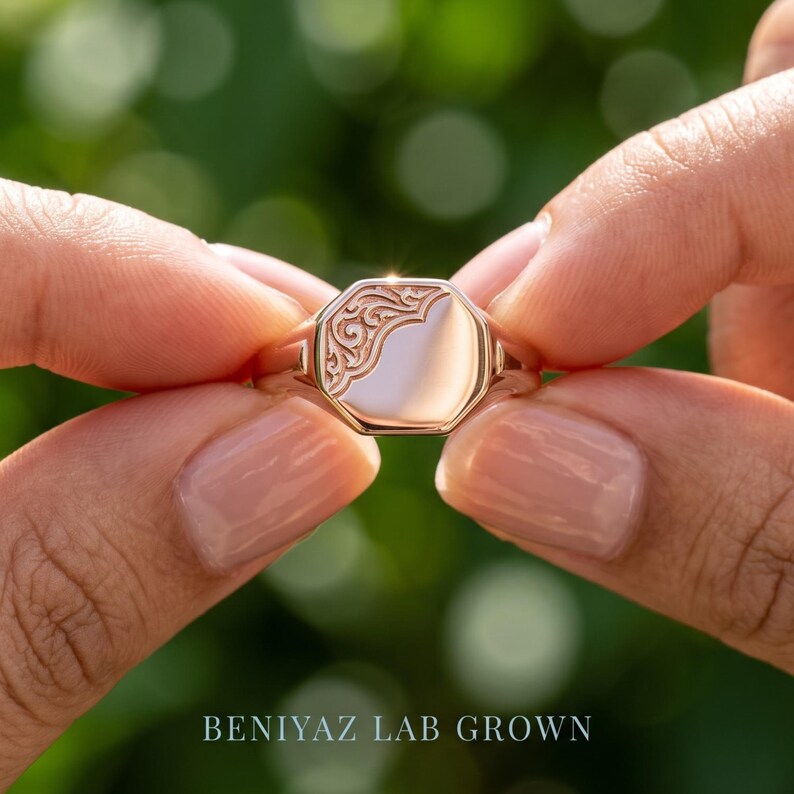 Close up engraved oval signet ring held by hand showing decorative floral scrollwork relief and polished personalized face
