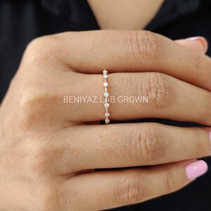 Close-up of a woman's hand wearing a dainty marquise moissanite wedding ring. The polished slim band and sparkling gemstones create a refined minimalist jewelry style.