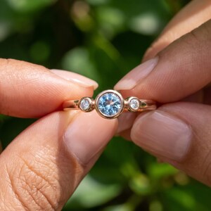 Blue gemstone three stone ring worn on hand showing the slim 1.30 mm solid gold band and bezel settings.