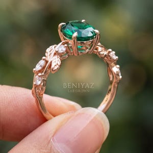 Close side view of leaf ring with oval lab created emerald, round accent stones and organic branch inspired setting.