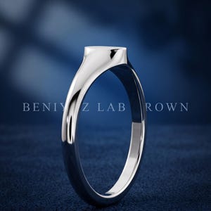 Side profile of petite oval signet ring on blue background showing tapered shank, slim band and high polish finish
