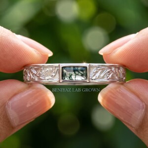 Puede incluir: Un anillo de tono plateado con una piedra preciosa rectangular de &aacute;gata musgosa en el centro. La banda est&aacute; decorada con un patr&oacute;n de hojas en relieve a ambos lados de la piedra. El texto BENIYAZ LAB GROWN aparece bajo el anillo.