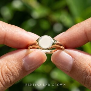 Close up round signet ring held by hand showing plain circular face, high polish finish and thin tapered signet shank