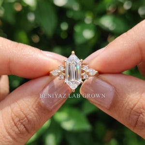 Front view of hexagon step cut lab grown diamond ring held by hand with marquise and round side stones in a seven stone design