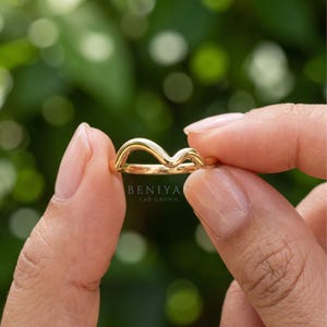 Hand held side view of a minimalist curved contour ring showing the polished gold finish and soft wishbone shape.