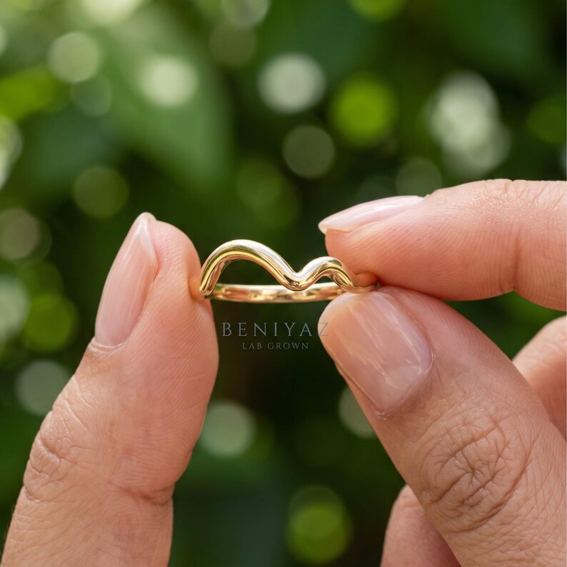 Hand held side view of a minimalist curved contour ring showing the polished gold finish and soft wishbone shape.