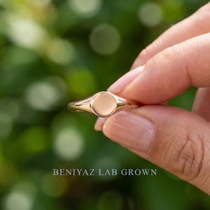 Round signet ring held by hand with plain polished circular face, thin tapered shank and minimalist everyday design