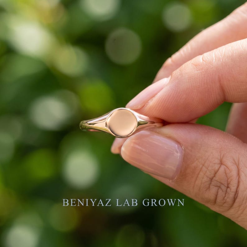 Round signet ring held by hand with plain polished circular face, thin tapered shank and minimalist everyday design
