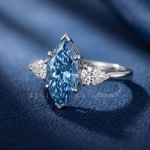Side angle studio view of an elongated blue marquise diamond ring showing the pear side stones and prong setting.
