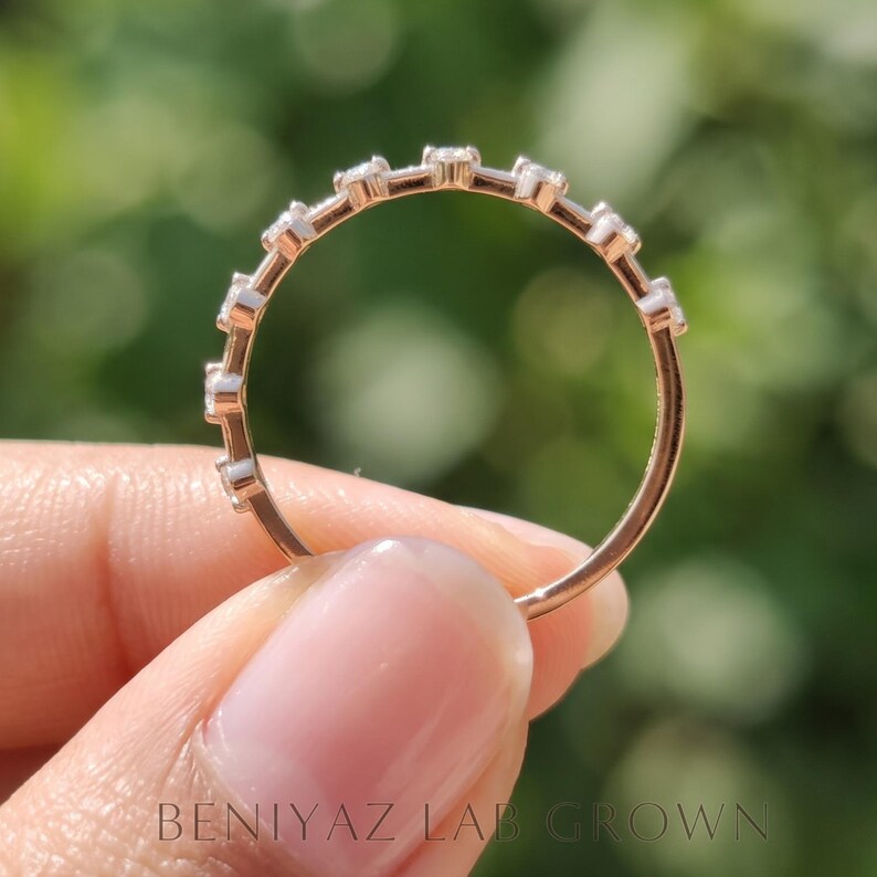Full circular view of a moissanite wedding band held between fingertips. The photograph highlights the polished ring shank, delicate marquise gemstone setting and slender band profile.