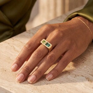 Hand wearing a modern teal sapphire signet ring with emerald cut teal sapphire and round green sapphire in a bold two stone statement design