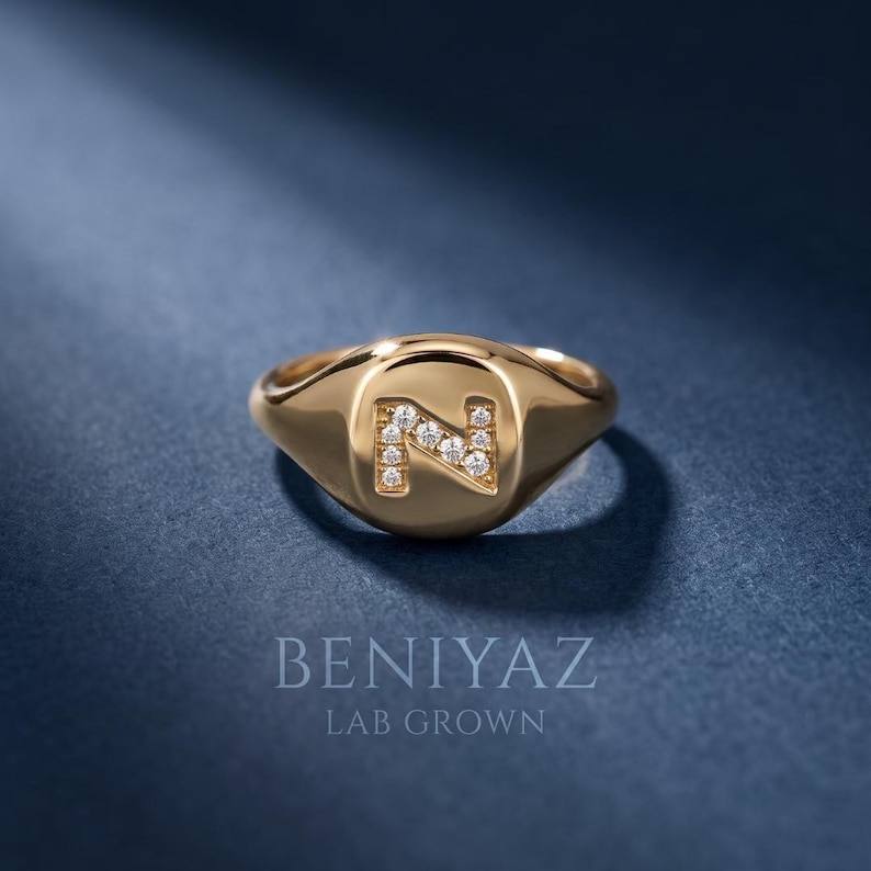 Custom initial N diamond signet ring in solid 14K yellow gold, featuring sparkling lab grown diamonds set into the letter N, photographed on a luxury deep blue background.