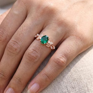 Emerald ring for women worn on finger, showing oval green gemstone center and detailed botanical leaf setting.