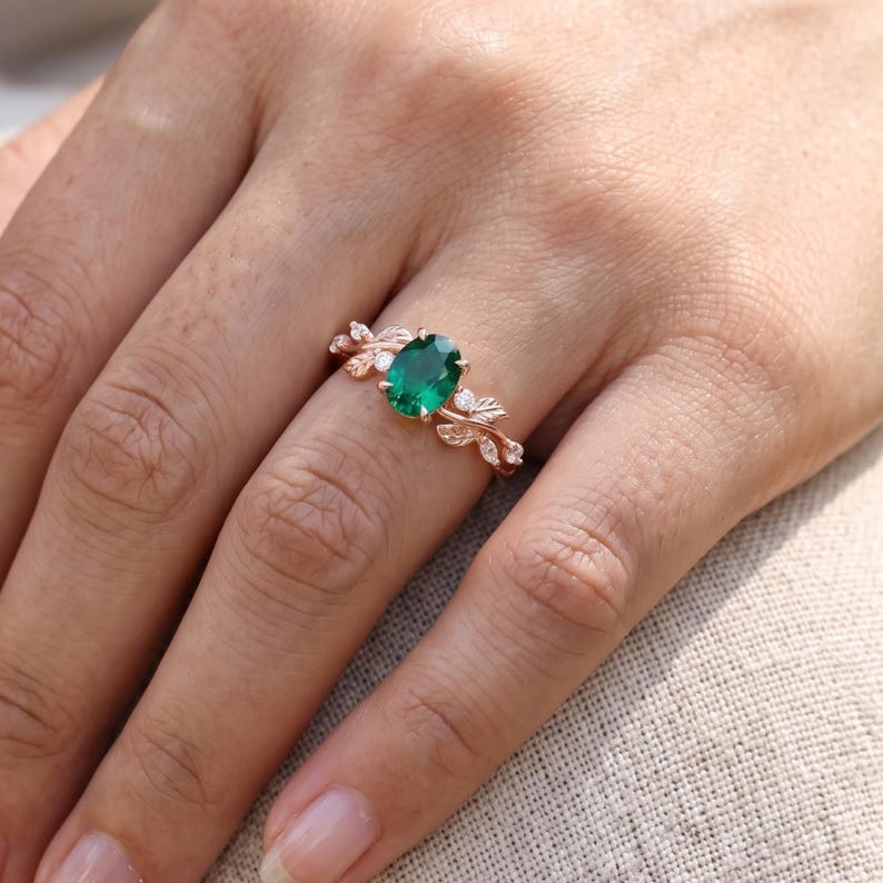 Emerald ring for women worn on finger, showing oval green gemstone center and detailed botanical leaf setting.
