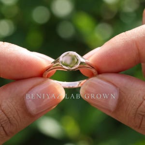 Close up side view of round signet ring held between fingers showing blank polished face and slim tapered shoulders