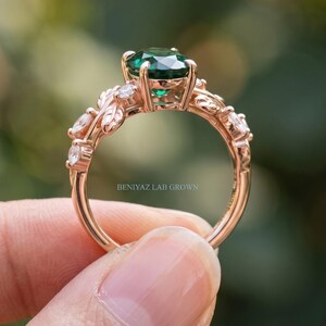 Botanical engagement ring with oval lab created emerald and detailed branch and leaf shoulders shown in natural light.