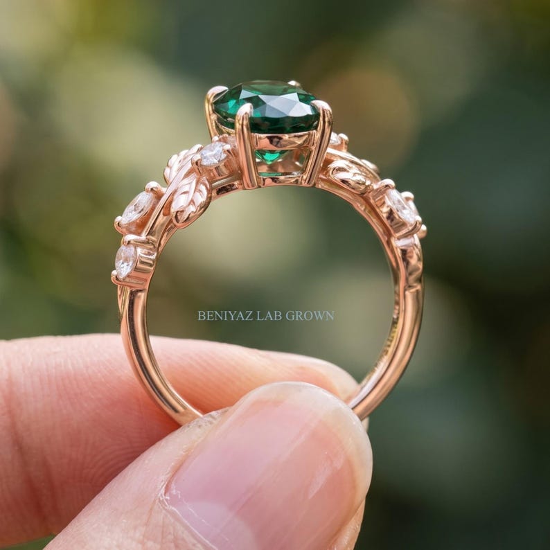 Botanical engagement ring with oval lab created emerald and detailed branch and leaf shoulders shown in natural light.