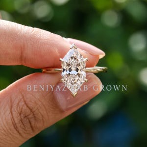 Op de afbeelding: Een gouden ring met een centrale steen in marquise-slijpvorm, vastgehouden door zes pootjes. De ringband is dun en van gepolijst goud. De tekst BENIYAZ LAB GROWN is zichtbaar in het midden van de afbeelding, over de steen en de ringband heen.
