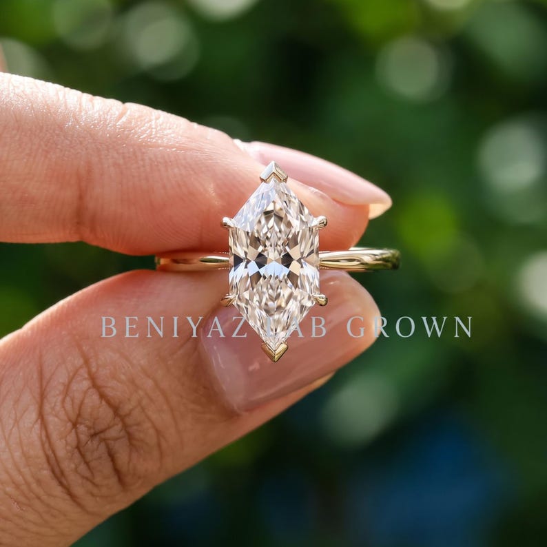 Op de afbeelding: Een gouden ring met een centrale steen in marquise-slijpvorm, vastgehouden door zes pootjes. De ringband is dun en van gepolijst goud. De tekst BENIYAZ LAB GROWN is zichtbaar in het midden van de afbeelding, over de steen en de ringband heen.