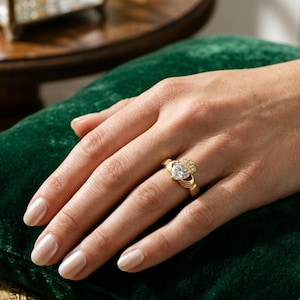 Studio close-up of a heart cut lab grown diamond Claddagh engagement ring on blue fabric with yellow gold detailing.
