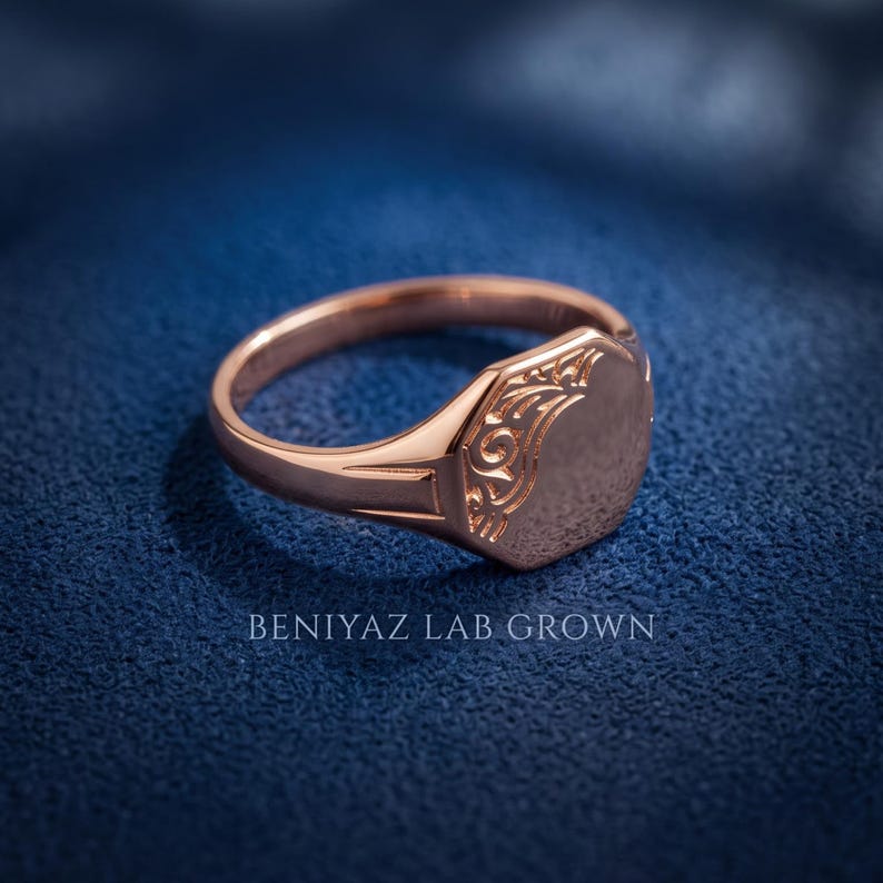 Rose gold oval signet ring on blue background featuring polished personalized face, ornate floral shoulders and tapered shank