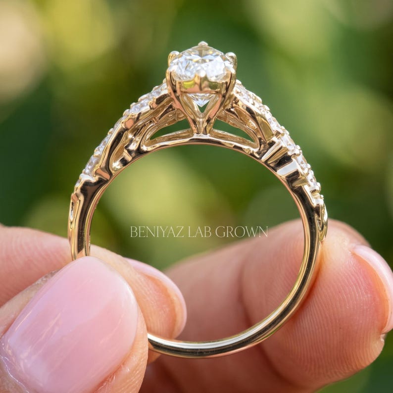 Full side profile of a marquise diamond engagement ring held upright between fingertips. The photograph highlights the elevated center diamond setting, intricate gallery design, decorative leaf shaped side accents and slender polished yellow gold shank.