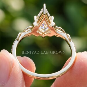 Rear view of a kite cut diamond engagement ring held upright outdoors. The photograph reveals the open gallery beneath the raised geometric center stone, detailed prong structure and decorative pavé band, with the full circular shank visible.