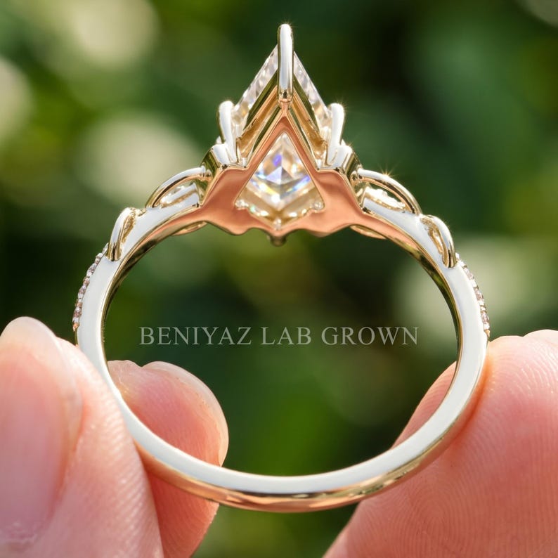 Rear view of a kite cut diamond engagement ring held upright outdoors. The photograph reveals the open gallery beneath the raised geometric center stone, detailed prong structure and decorative pavé band, with the full circular shank visible.