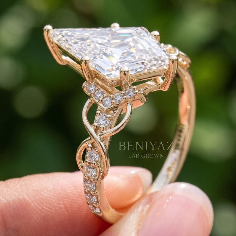 Full upright profile of a kite shaped lab grown diamond engagement ring against soft green foliage. The image shows the tall center stone setting, detailed gallery, sparkling infinity inspired shoulders and slim circular gold tone shank.