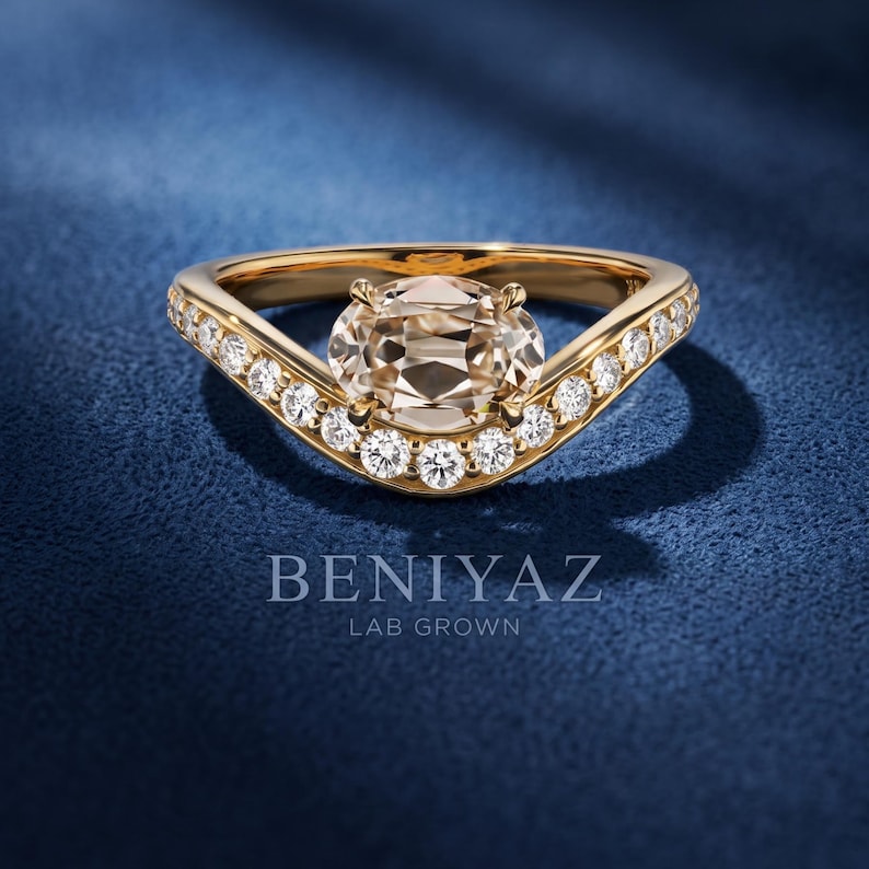 Oval cut lab grown diamond engagement ring in yellow gold with a modern bypass crossover design and pavé set round side diamonds, photographed on a deep navy blue luxury background.