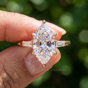 Three quarter hand held view of elongated Dutch marquise lab grown diamond ring with side stones and prong setting