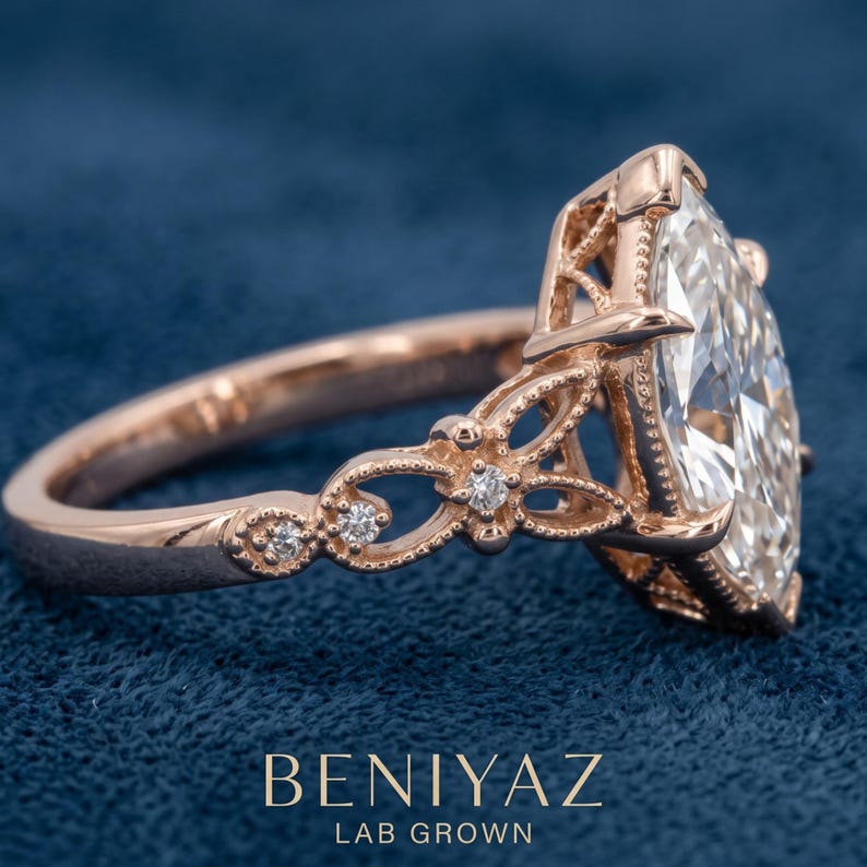May include: A rose gold ring featuring a large marquise-cut center stone and intricate filigree detailing along the band, accented with small round diamonds. The text BENIYAZ LAB GROWN is printed at the bottom of the image in white lettering.