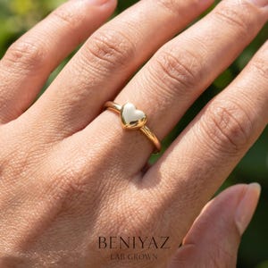 Puffy heart ring worn on finger, showing the dainty minimalist design and small polished heart centerpiece.