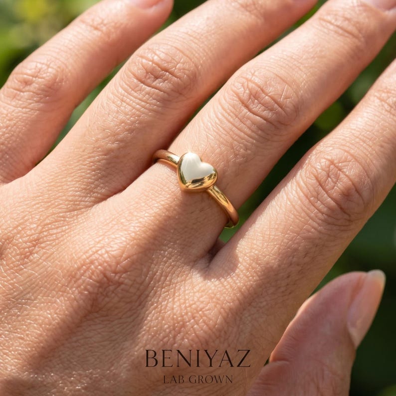 Puffy heart ring worn on finger, showing the dainty minimalist design and small polished heart centerpiece.
