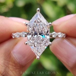 May include: A silver-toned ring featuring a large, elongated marquise-cut center stone held by six prongs. The band is accented with smaller, round-cut stones along the sides. The text BENIYAZ LAB GROWN is printed at the bottom.
