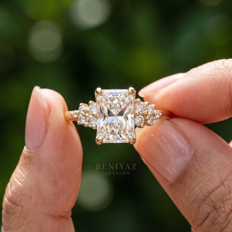May include: A gold ring featuring a large rectangular radiant-cut center stone flanked by three smaller round-cut stones on each side. The text BENIYAZ LAB GROWN is printed below the ring. The band is a polished yellow gold metal finish.