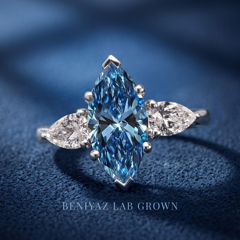 Front studio close-up of a blue marquise lab grown diamond three stone engagement ring with symmetrical pear cut side diamonds.