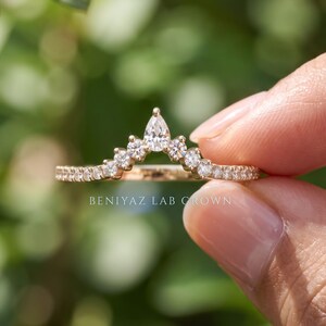 Detailed hand photo of a 0.30 CT TW lab grown diamond wedding band in 14K yellow gold with a curved chevron shape and pear diamond center accent