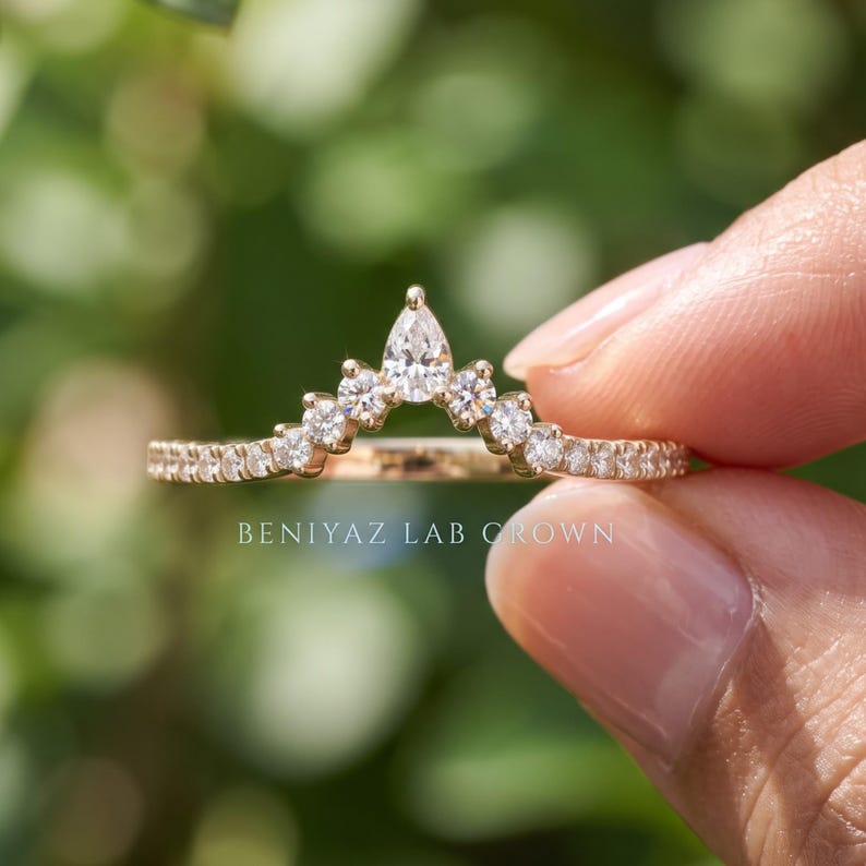 Detailed hand photo of a 0.30 CT TW lab grown diamond wedding band in 14K yellow gold with a curved chevron shape and pear diamond center accent