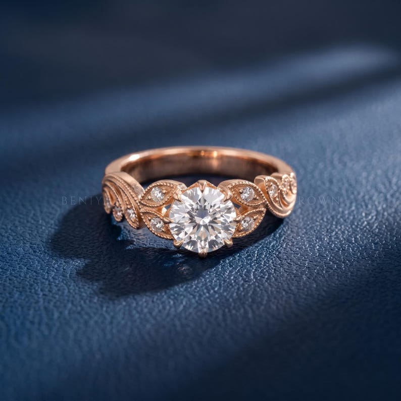 Rose gold vintage engagement ring featuring a round lab grown diamond center stone with intricate leaf detailing, milgrain texture and small side diamonds on a romantic floral band.