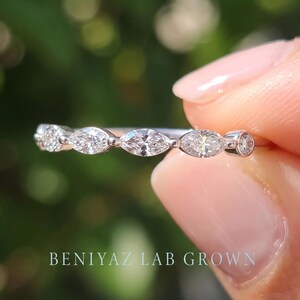 Macro front view of a delicate marquise diamond band held between fingertips. Three brilliant marquise cut lab grown diamonds with round accent stones form an elegant five-stone design on a slim polished metal ring.