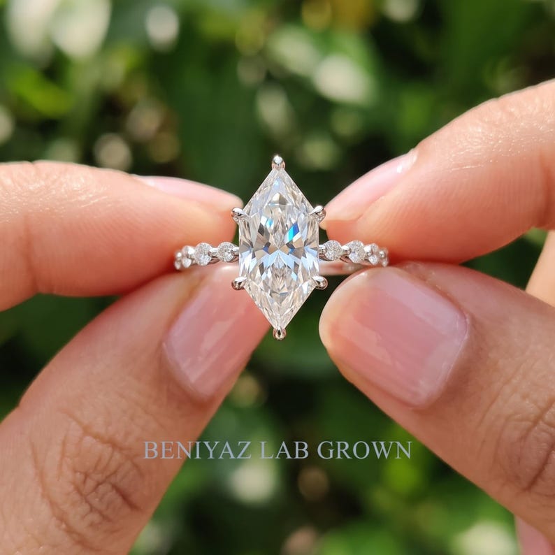 Detailed macro view of a Dutch marquise diamond engagement ring held between fingertips, showing the brilliant center diamond, six prong setting and symmetrical diamond accent design.