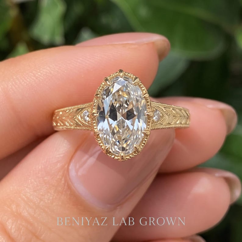 Macro front view of an oval diamond engagement ring held between fingertips. The sparkling oval center gemstone, smaller diamond accents and detailed band are shown against a soft green background.