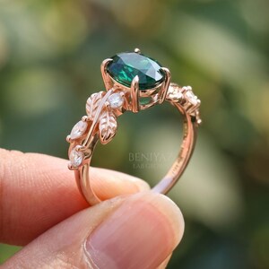 Branch ring close up featuring oval lab emerald center stone, round sparkling accents and detailed botanical shoulders.