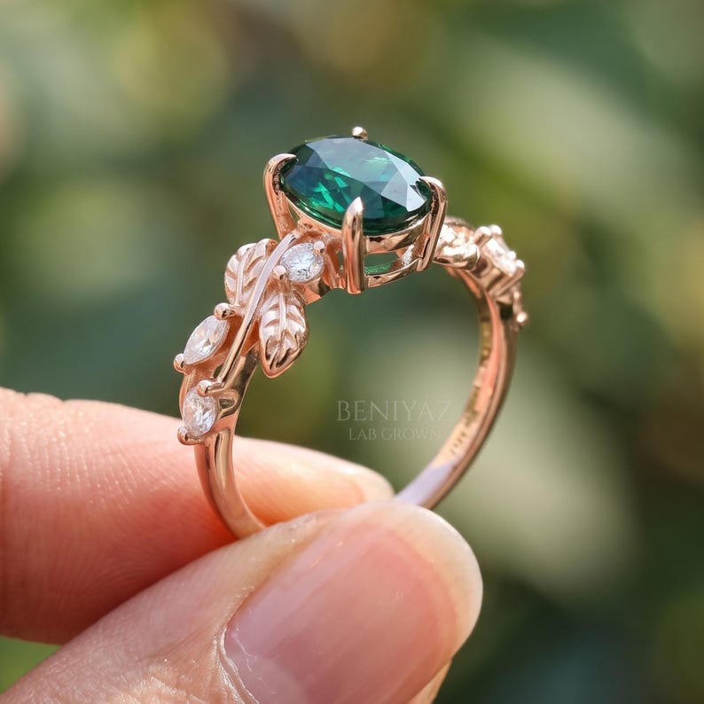 Branch ring close up featuring oval lab emerald center stone, round sparkling accents and detailed botanical shoulders.