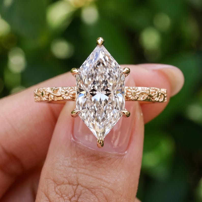 Hand held marquise lab grown diamond ring showing the elongated center stone and detailed floral gold band.